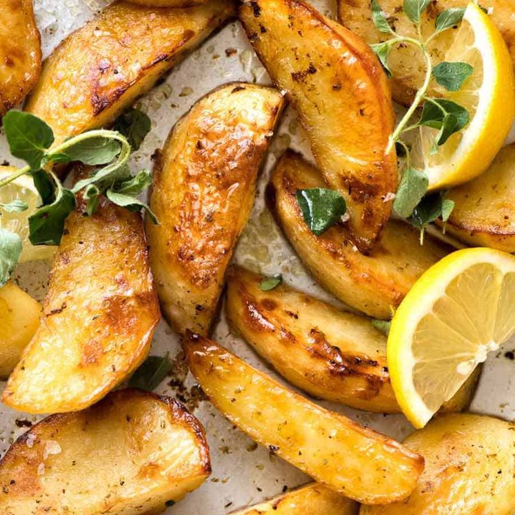 Close up of Greek Lemon Potatoes garnished with fresh oregano and lemon wedges