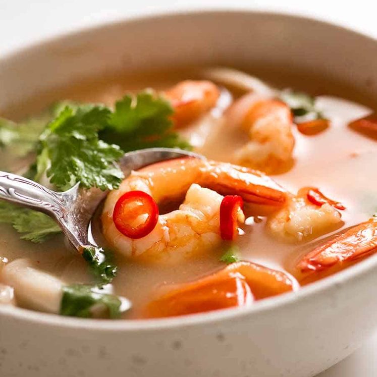 White bowl with Tom Yum Soup (Thai soup) with prawns / shrimp, mushrooms, tomato and garnished with coriander and chilli