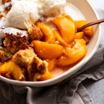 Peach Cobbler in a bowl topped with vanilla ice cream