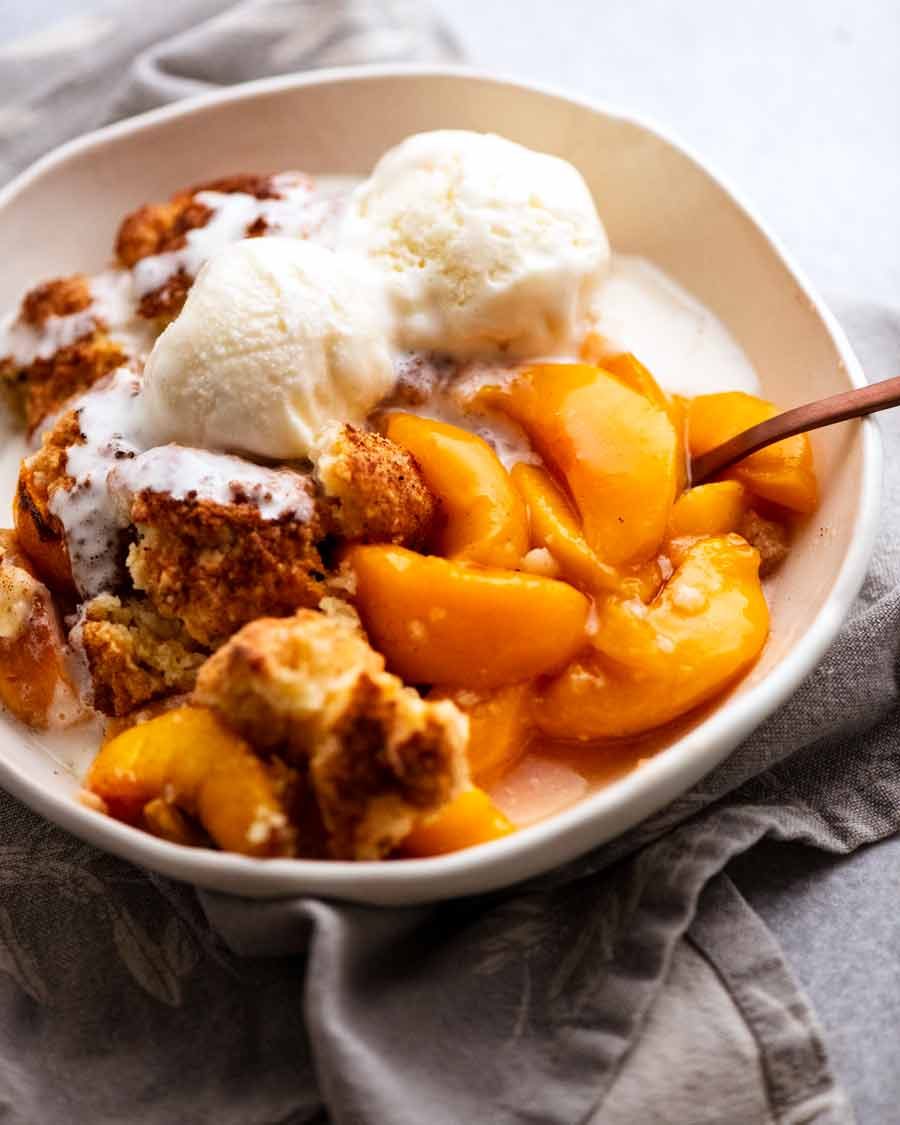 Peach Cobbler in a bowl topped with vanilla ice cream