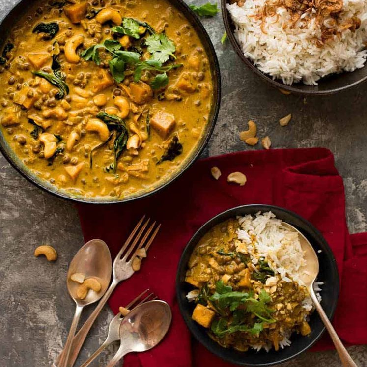 Tablescape overhead photo of Coconut Curry with Lentils & Pumpkin in a dark bowl with a side of rice, ready to be served.