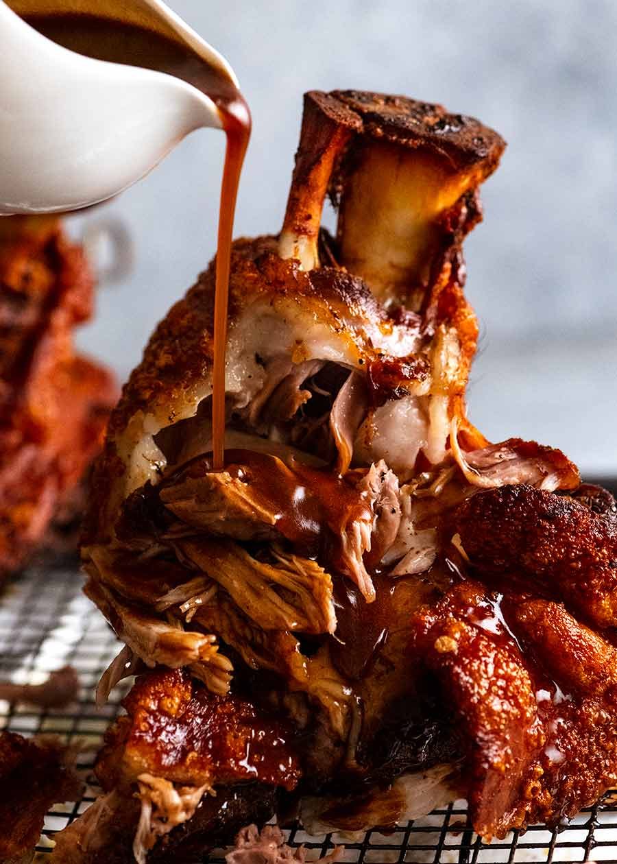 Photo of pouring beer gravy over German Pork Knuckle (Schweinshaxe) with ultra Crispy Skin