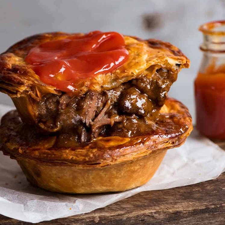 Two homemade Australian Meat Pies with tomato sauce, ready to be eaten