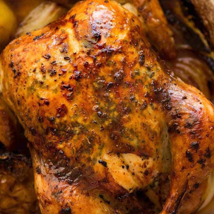 Overhead photo of golden Roast Chicken with crispy skin, fresh out of the oven, bathed in garlic-herb-lemon butter.