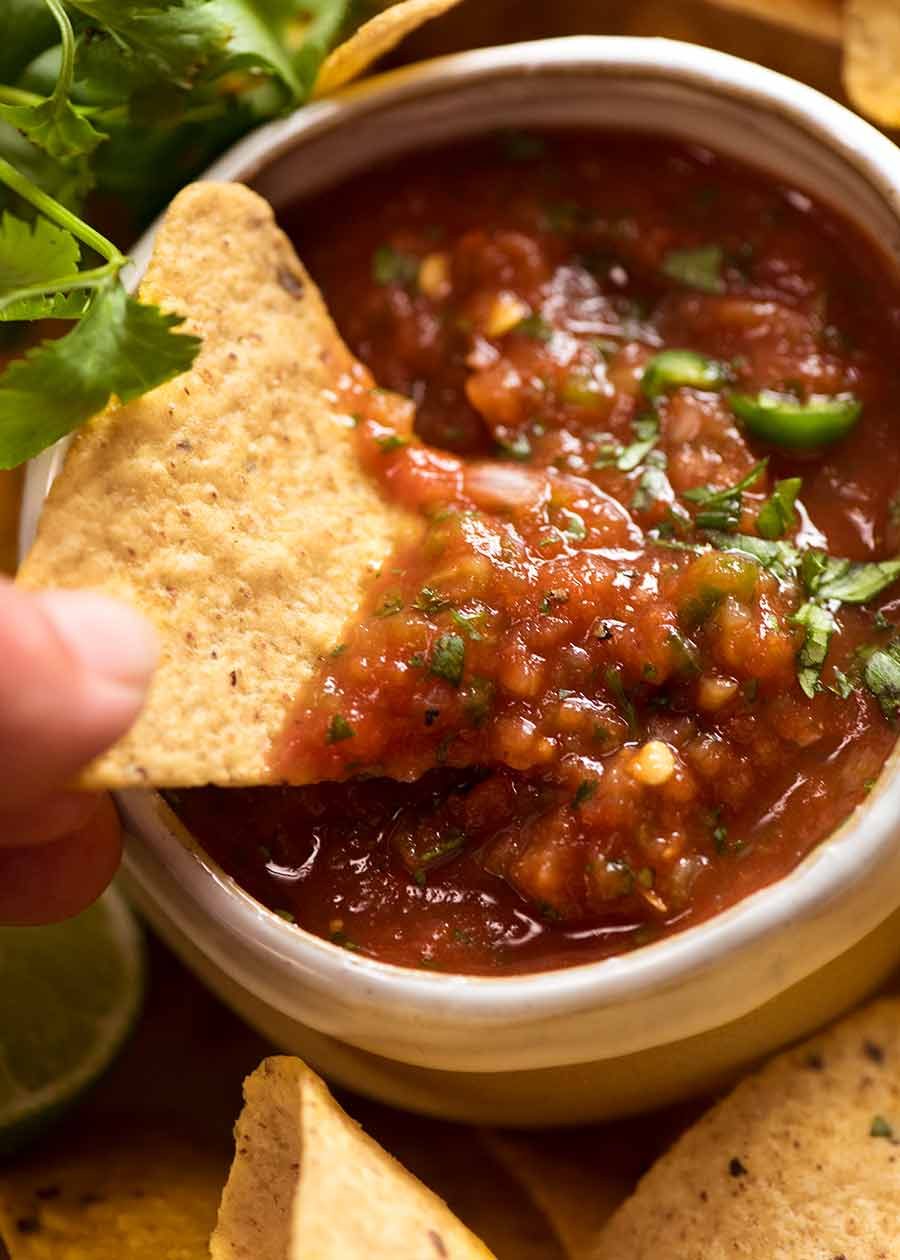 Close up of corn chip scooping up homemade salsa (Salsa recipe - restaurant style)