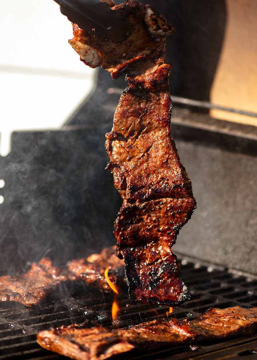 Tongs picking up a piece of Korean BBQ Marinated Beef Short ribs (Galbi) off the BBQ grill