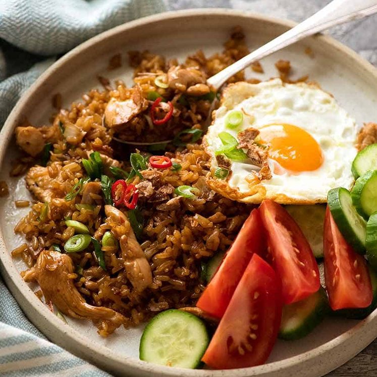 Nasi Goreng on a plate with a side of fried egg, tomato and cucumbers