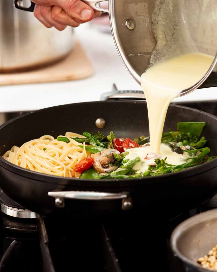 pasta-primavera-cream-sauce-pour Pouring cream sauce over Pasta Primavera